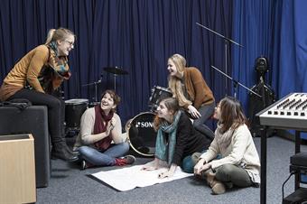 The picture shows a group of female students and a lot of instruments in music studio.